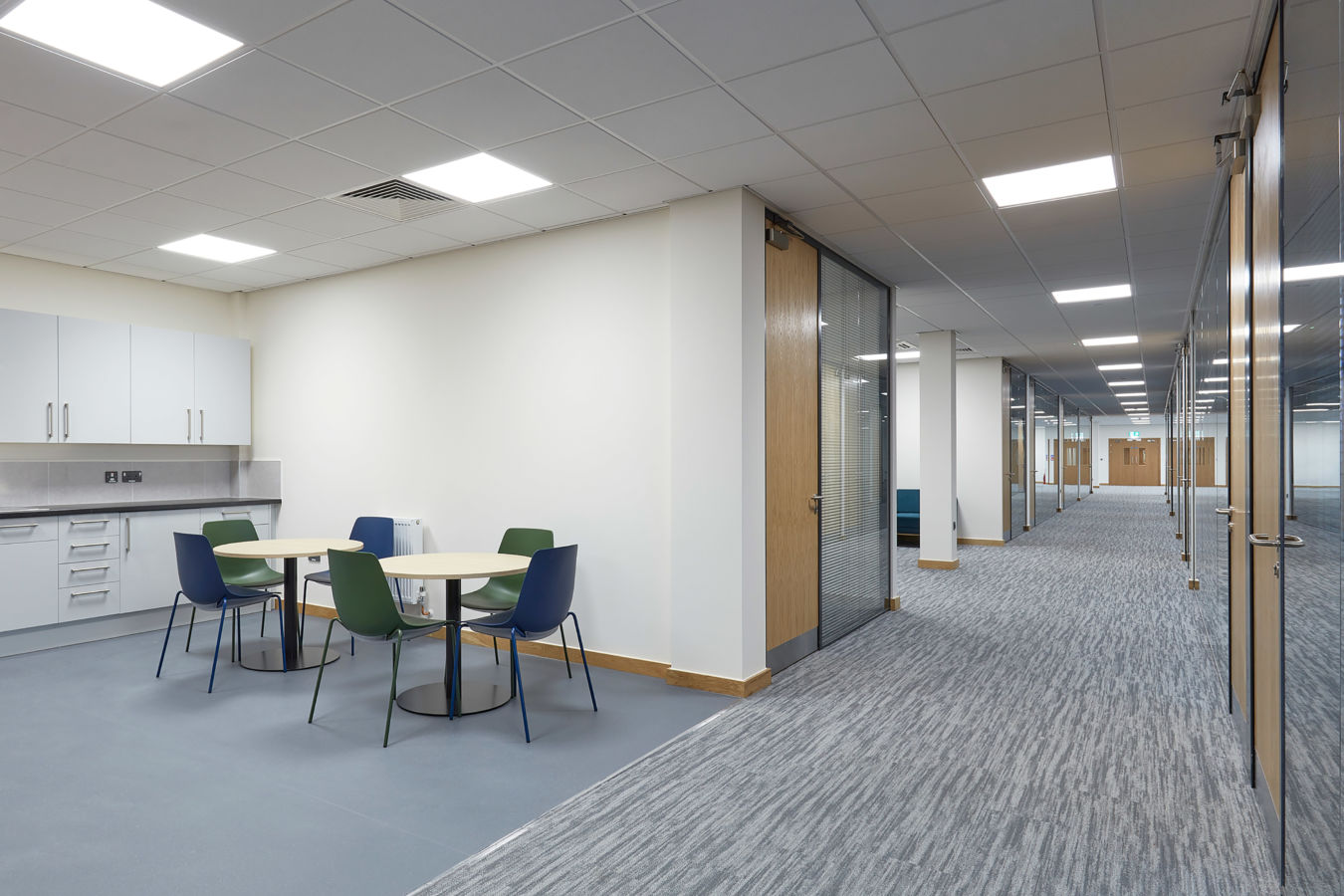 spacious, brightly lit office hallway with a variety of seating options, including a blue sofa and yellow chairs