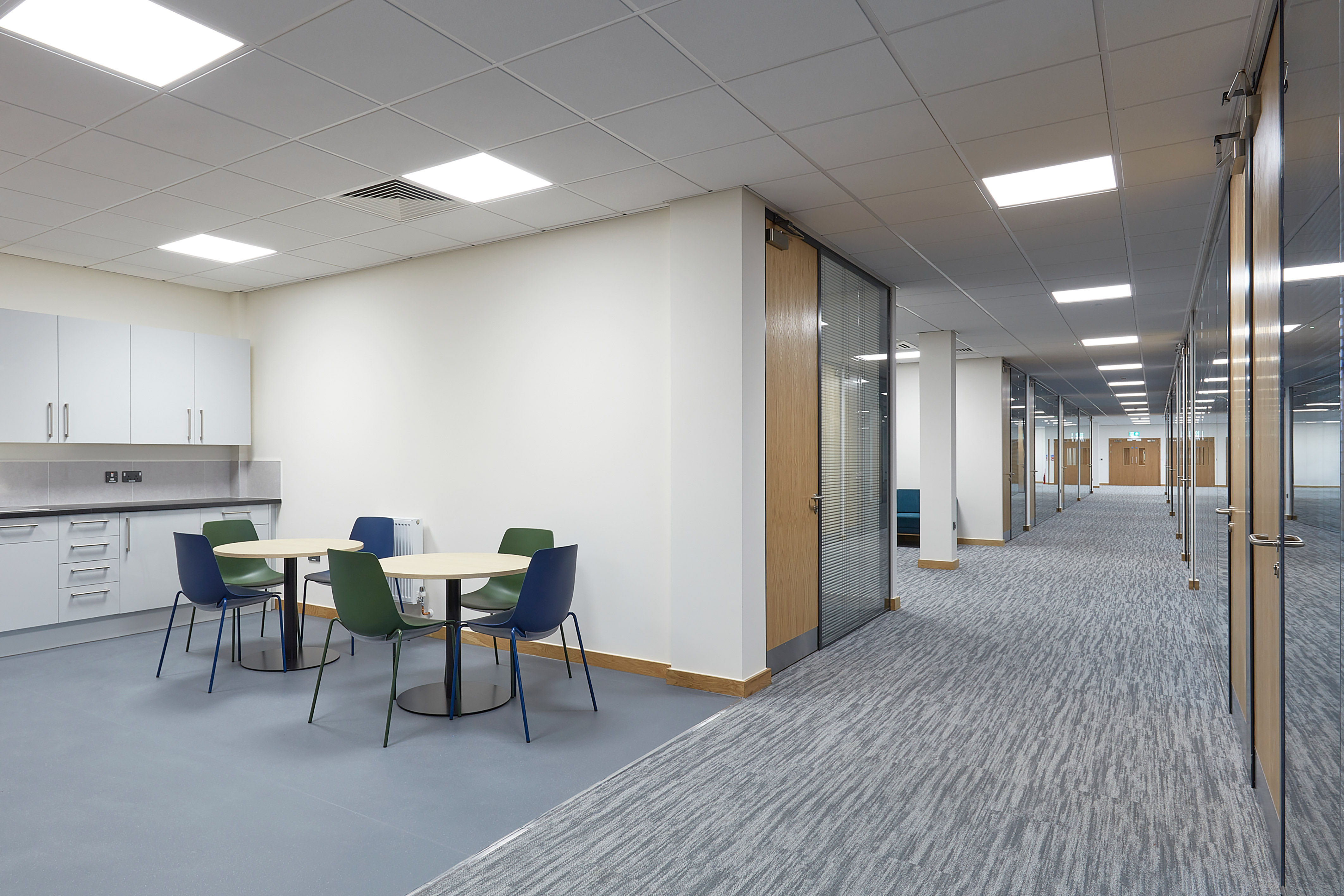 spacious, brightly lit office hallway with a variety of seating options, including a blue sofa and yellow chairs
