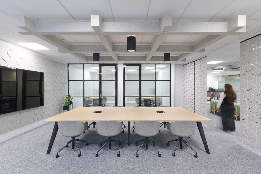 Contemporary conference room with a long wooden table, grey swivel chairs, geometric ceiling panels, and glass partition walls.