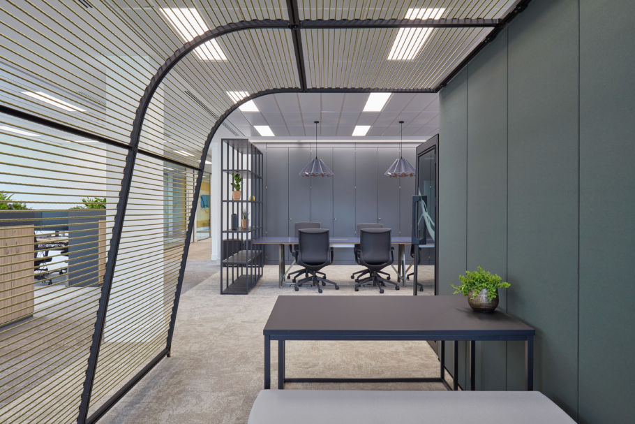 Modern office interior with open-plan workstations, black framed partitions, sleek furniture, and a semi-private meeting pod with overhead slatted canopy.