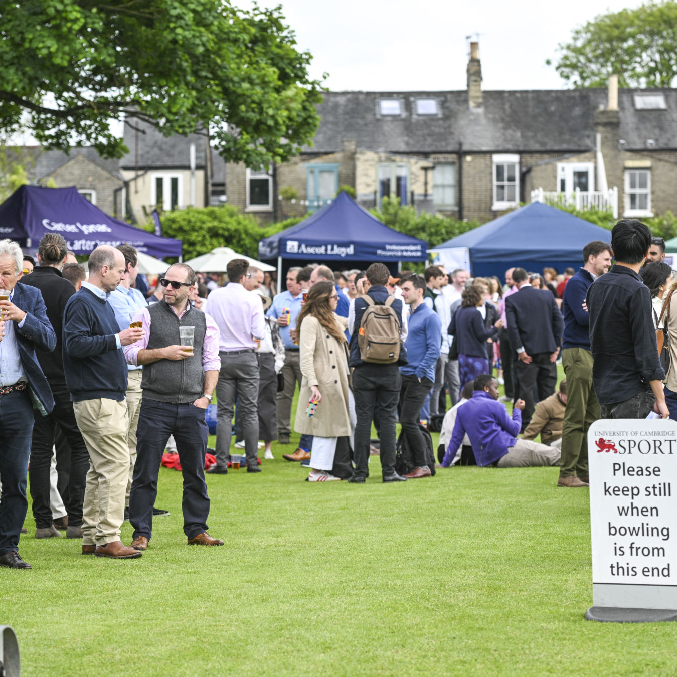 Man holding a microphone speaks outdoors at an event, surrounded by a crowd; "coel.co.uk" is written on a nearby blue canopy.