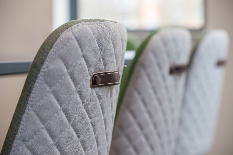 Close-up of three gray quilted chair backs with green edges and brown leather details, arranged in a row, conveying a modern, cozy ambiance