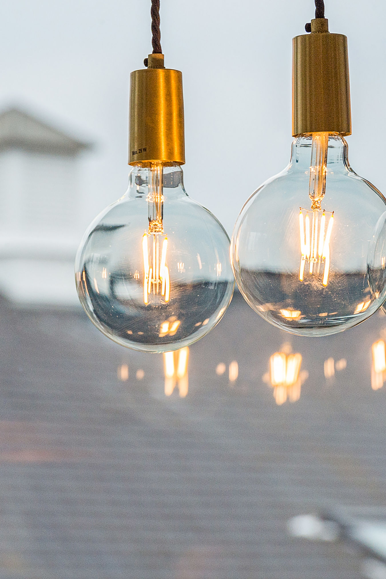 Two glowing light bulbs hang from twisted cords, set against a blurred, out-of-focus background featuring a rooftop.