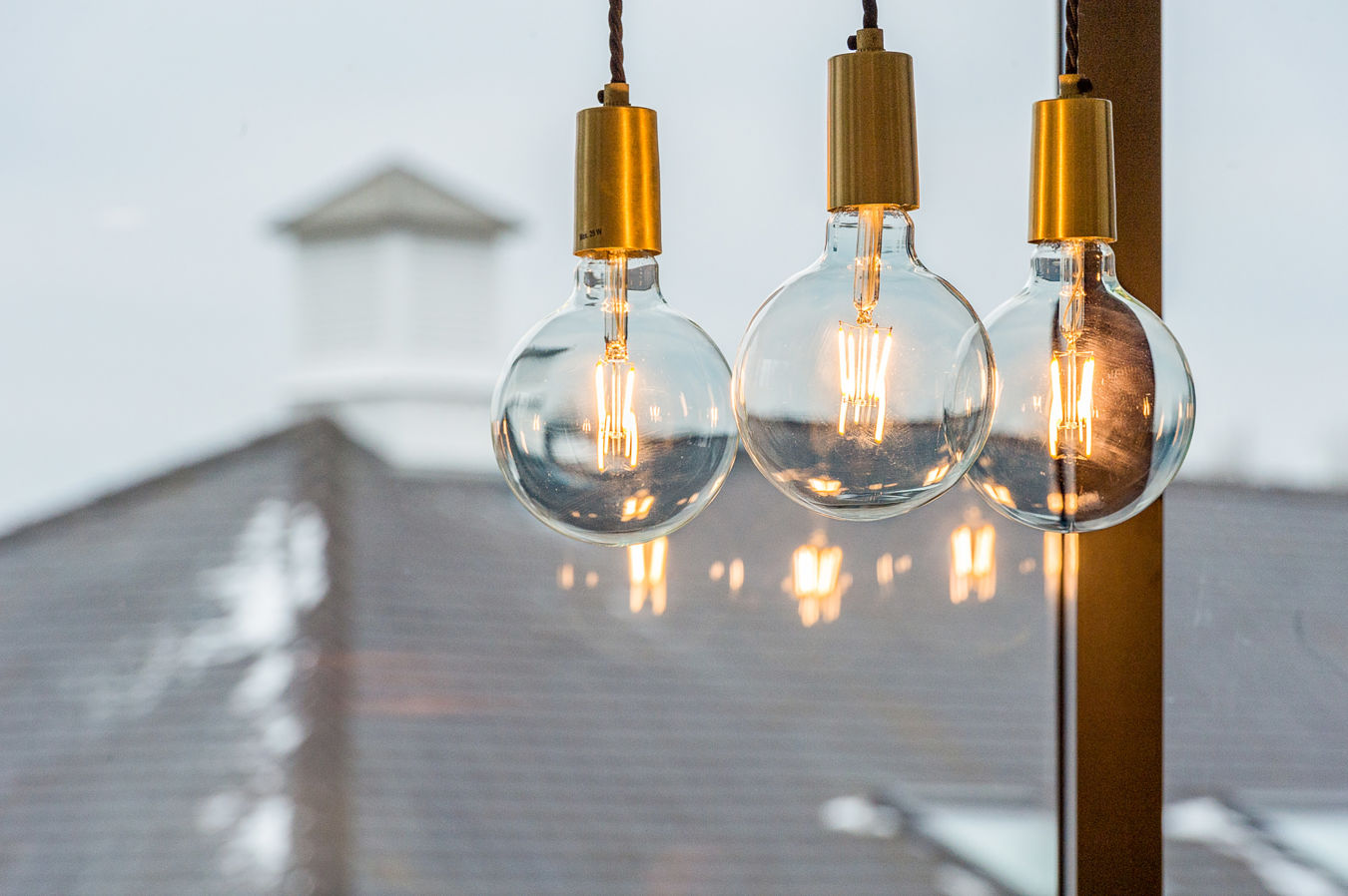 Two glowing light bulbs hang from twisted cords, set against a blurred, out-of-focus background featuring a rooftop.
