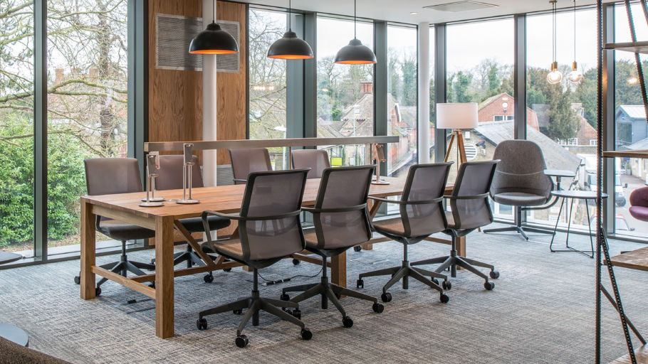  modern conference room with a wooden table, eight mesh chairs, and hanging lights. Large windows showcase trees and buildings, creating an open, airy feel