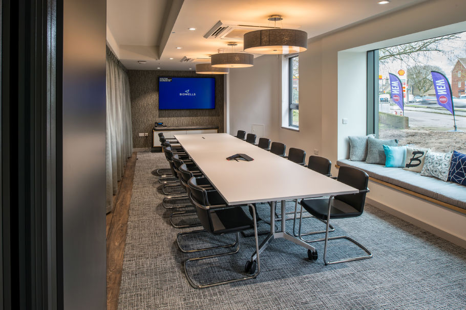 modern conference room with a long white table, black chairs, and a screen on the wall. Large window with a cushioned bench and decorative pillows