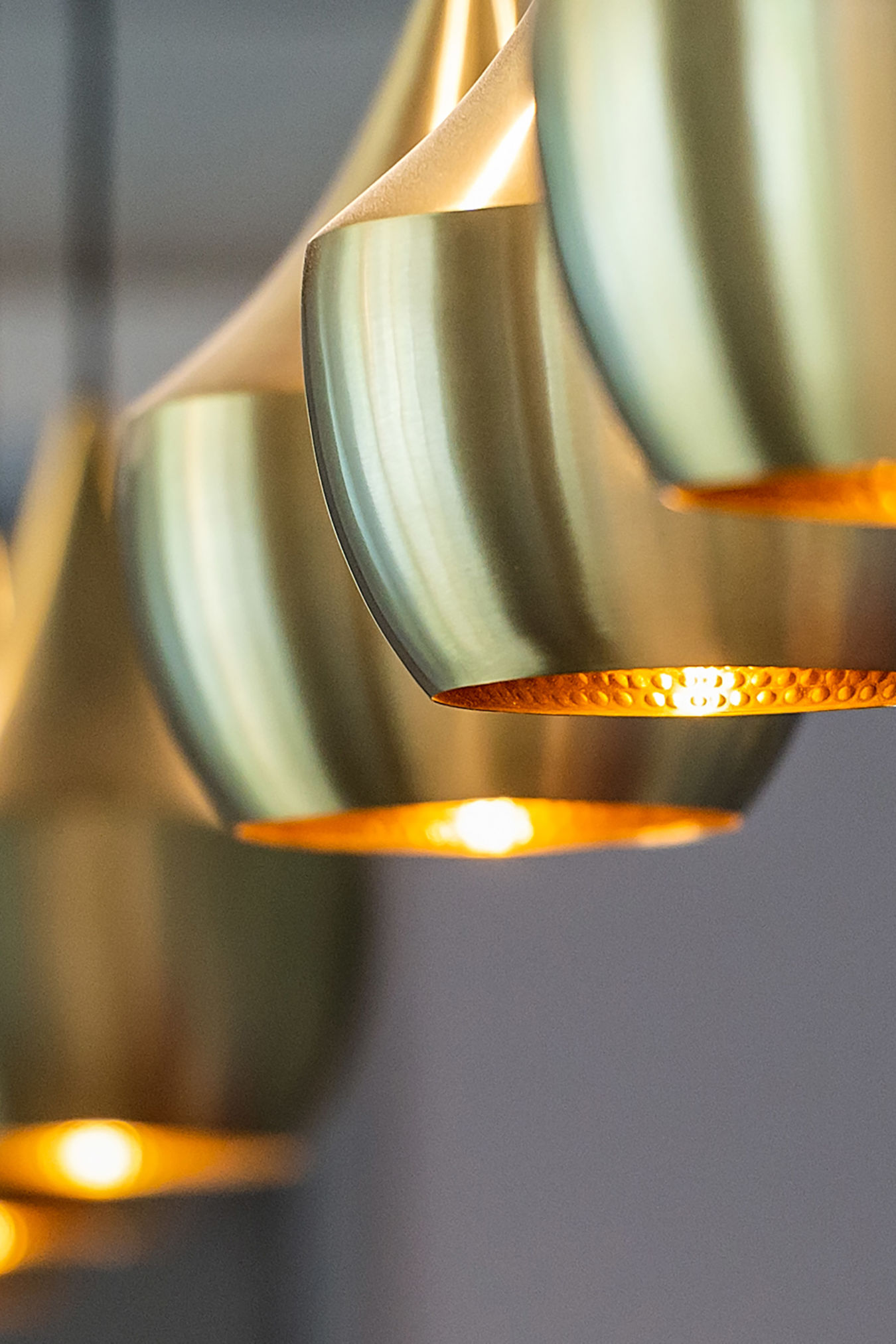Brass pendant lights are illuminated, casting a warm glow; they hang in a row, creating a modern, elegant ambience in a softly lit room.