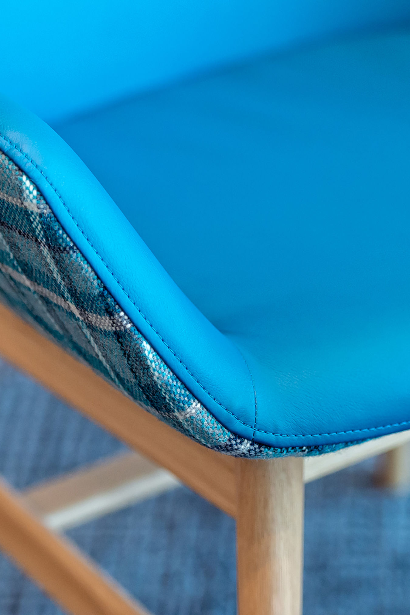 Blue-cushioned chair with a plaid-patterned fabric edge sits on wooden legs, positioned on a textured blue carpet.