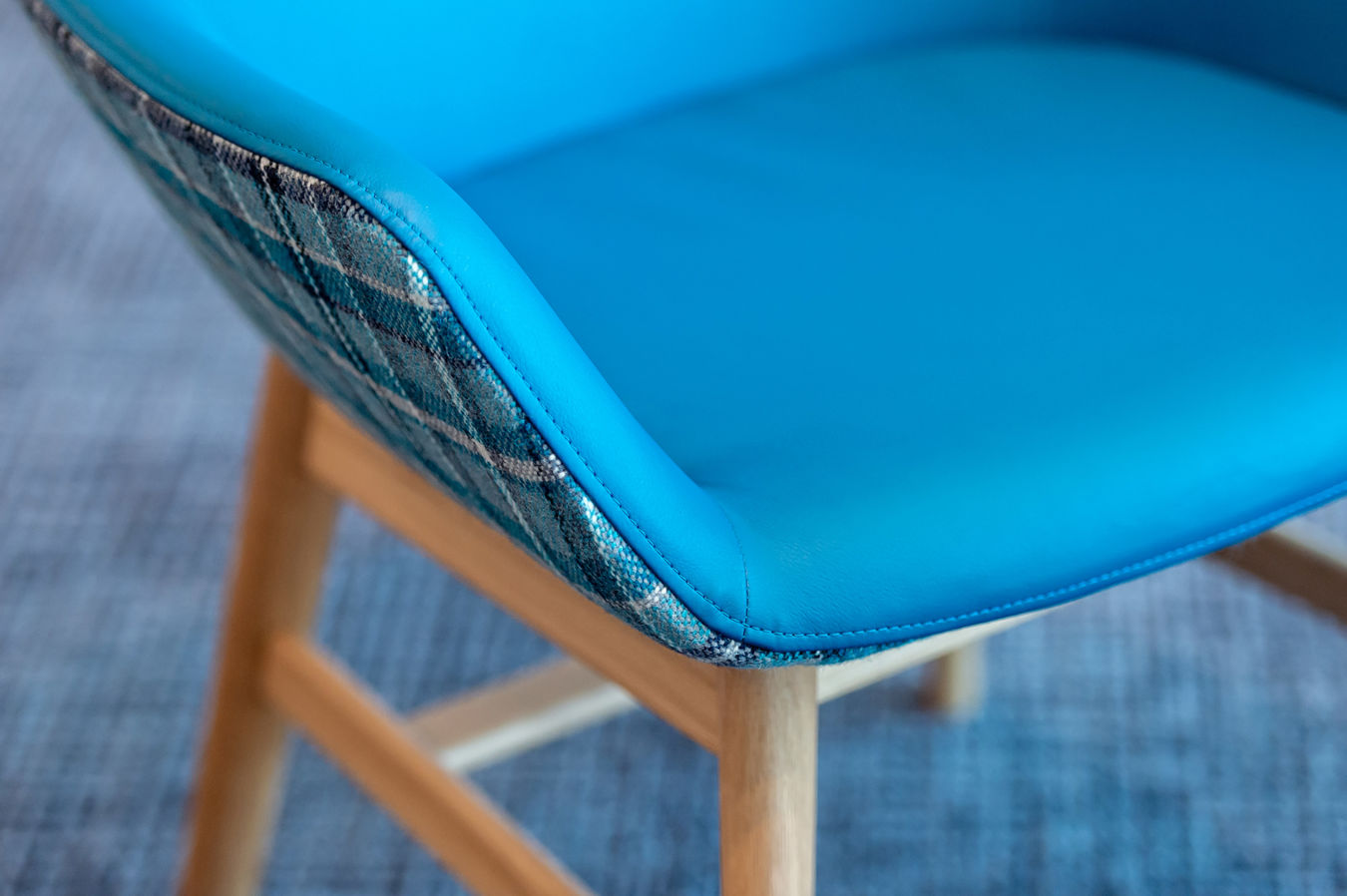 Blue-cushioned chair with a plaid-patterned fabric edge sits on wooden legs, positioned on a textured blue carpet.