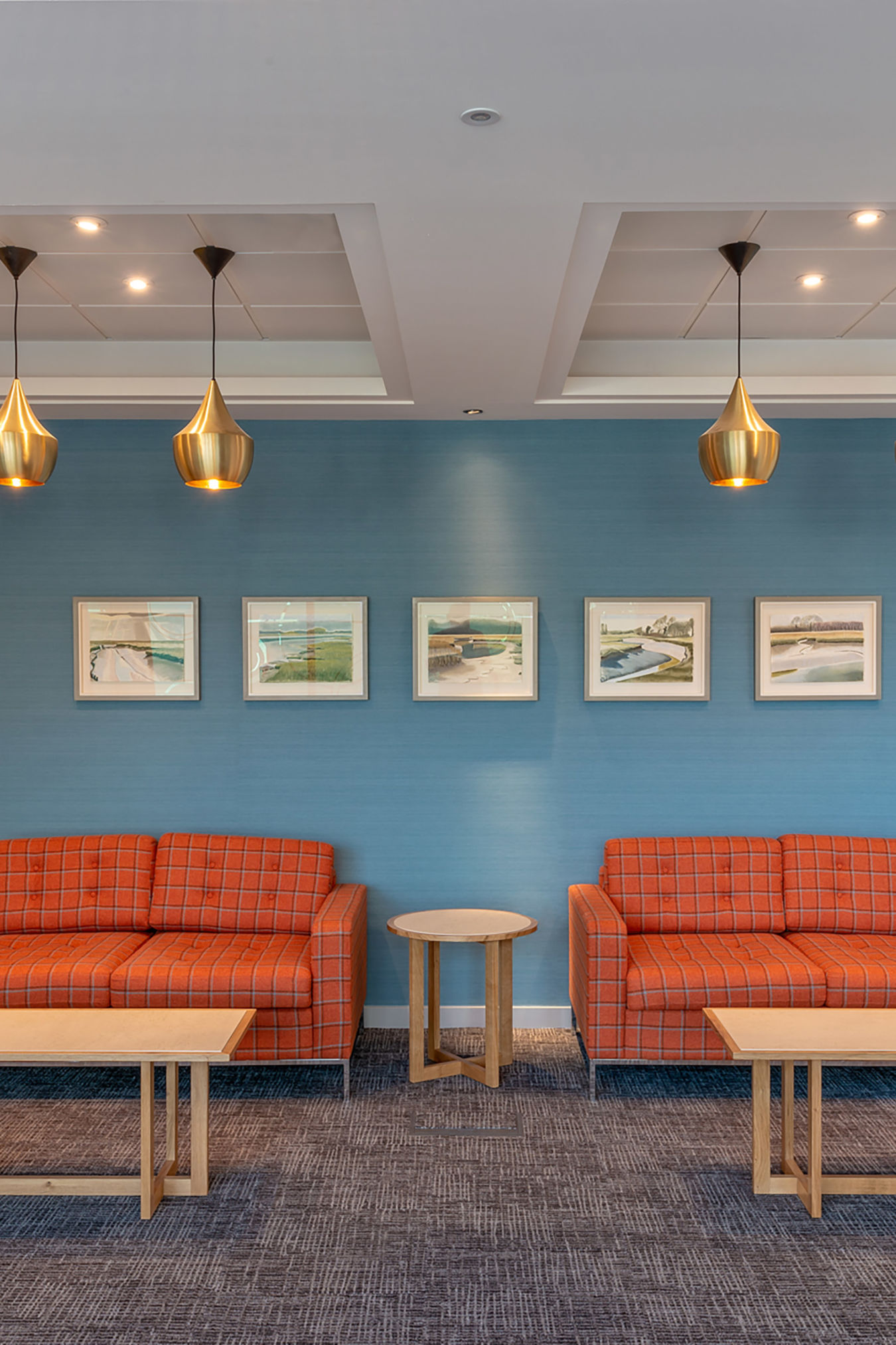 Stylish office lounge with twin orange sofas, pendant lighting, and blue accent wall, part of COEL’s furniture installation for Birketts in Ipswich.