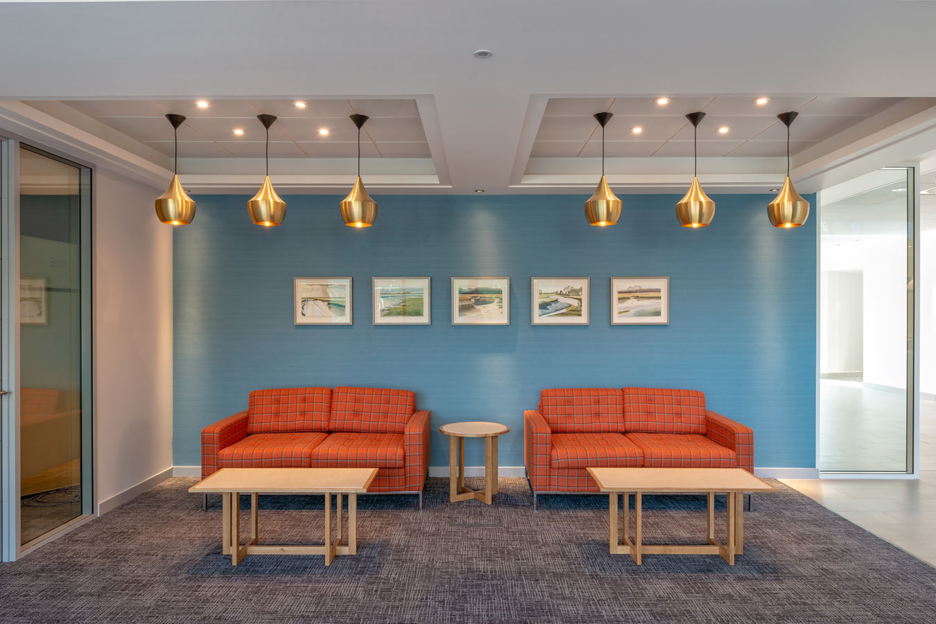 Stylish office lounge with twin orange sofas, pendant lighting, and blue accent wall, part of COEL’s furniture installation for Birketts in Ipswich.