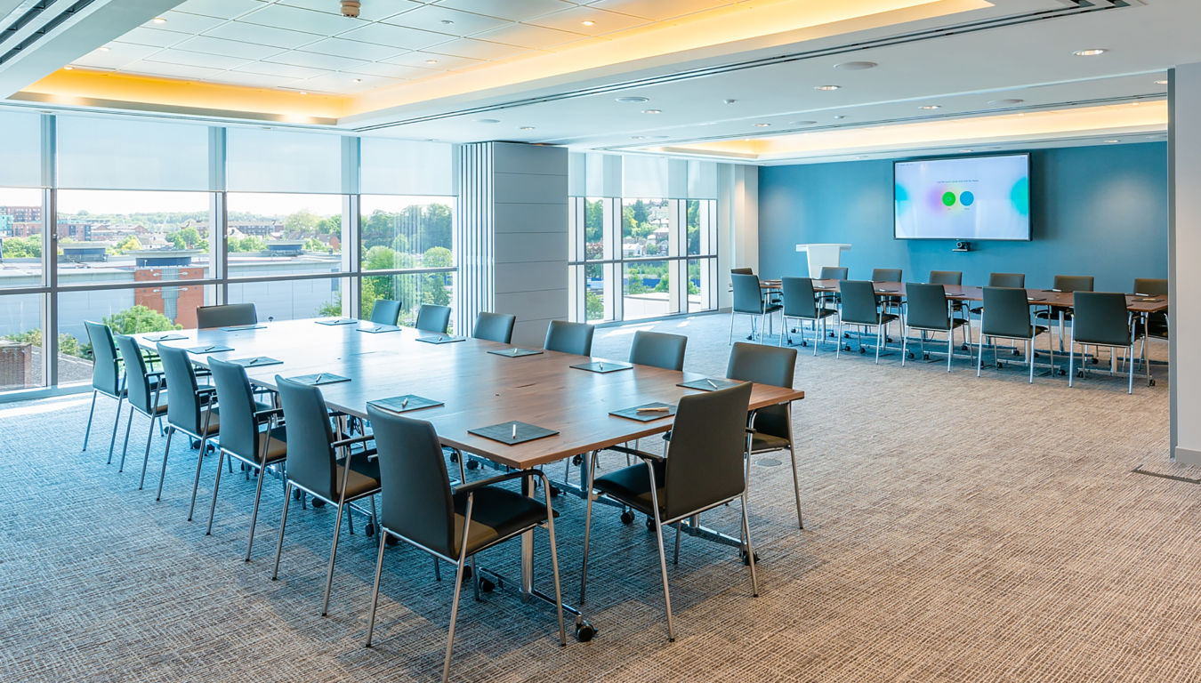 spacious, modern meeting room with large windows, multiple tables, chairs, and a presentation screen