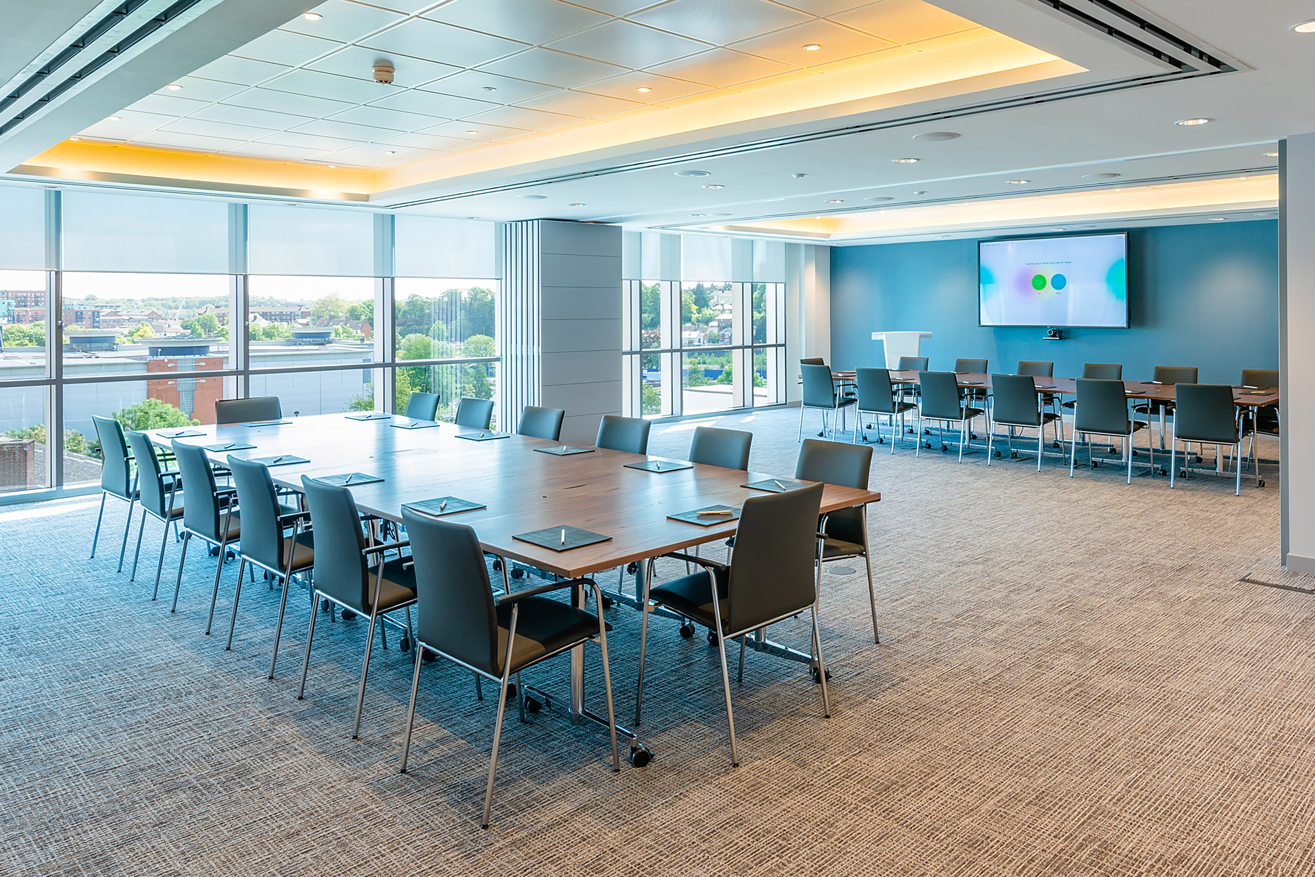 spacious, modern meeting room with large windows, multiple tables, chairs, and a presentation screen