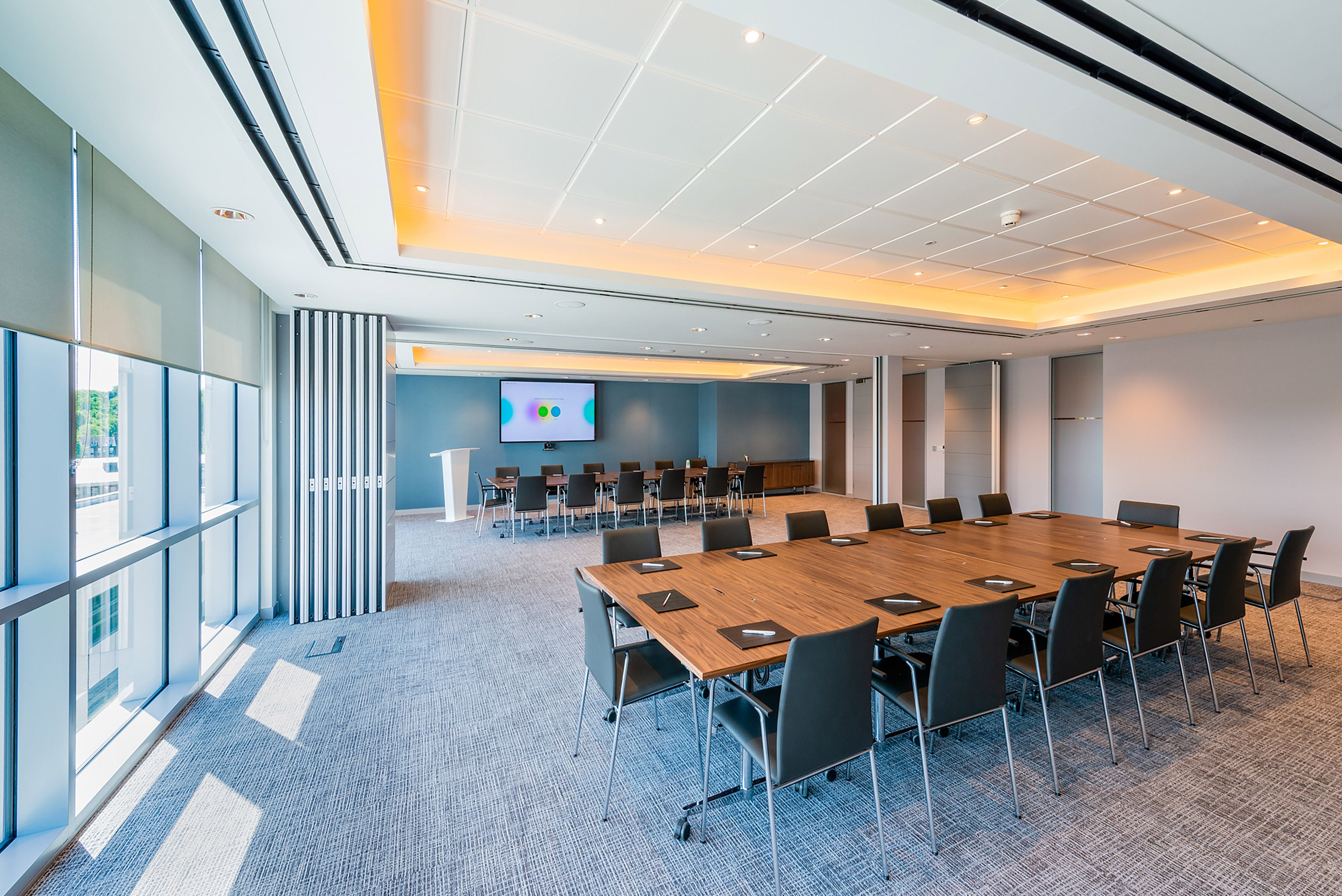 modern meeting room with a large wooden table, black chairs, a presentation screen, and large windows
