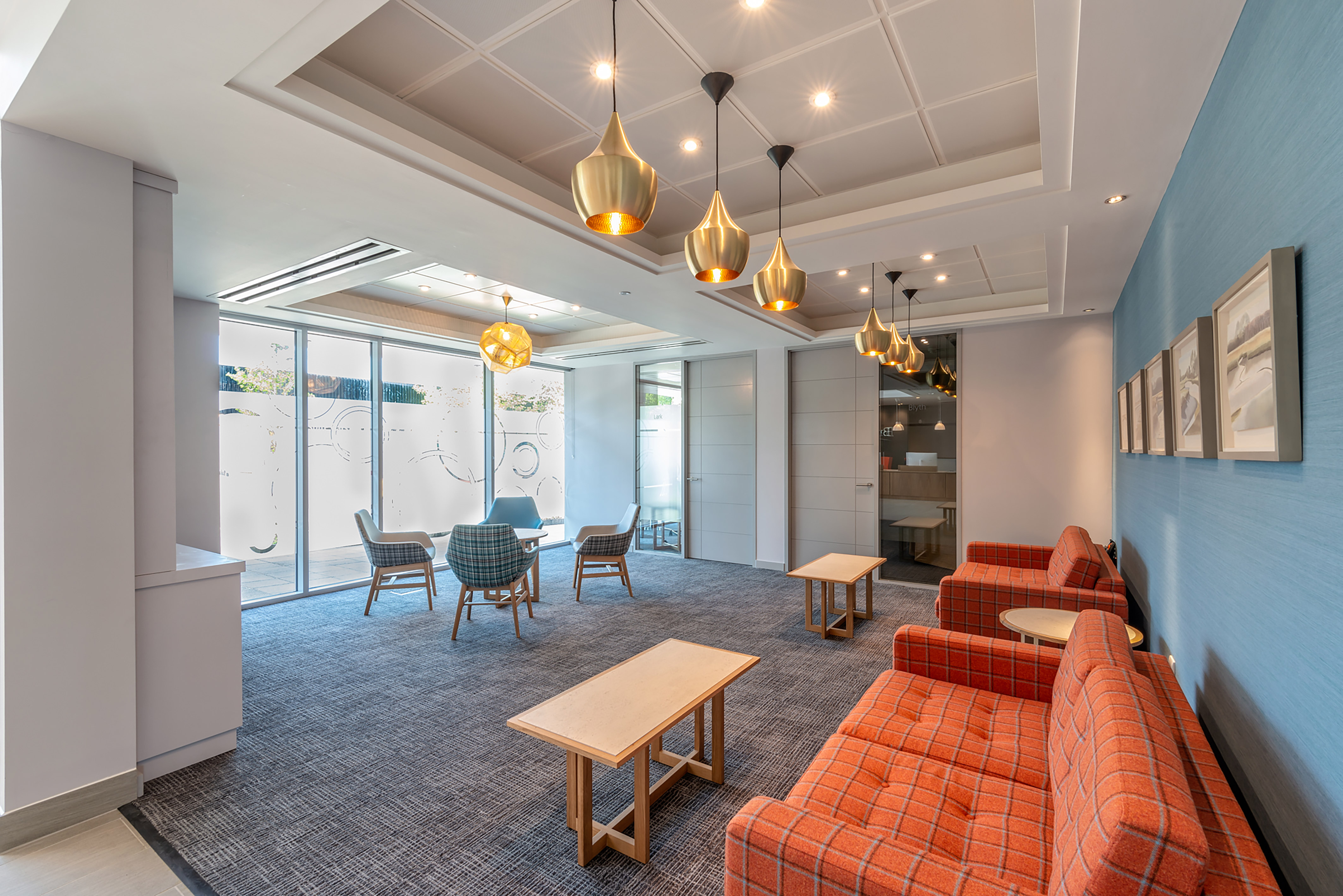 Vibrant office lounge area with orange seating, pendant lighting, and natural light, designed and furnished by COEL for Birketts in Ipswich.
