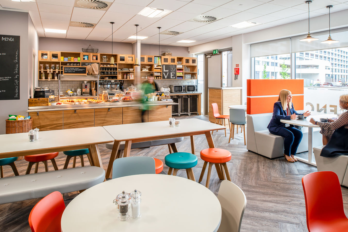 bustling cafe with a long counter, diverse seating, and two women conversing at a booth