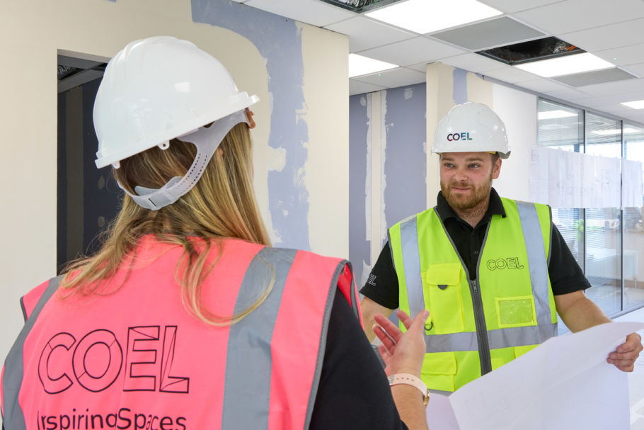 Two construction professionals in COEL-branded safety gear reviewing plans inside a building under renovation.