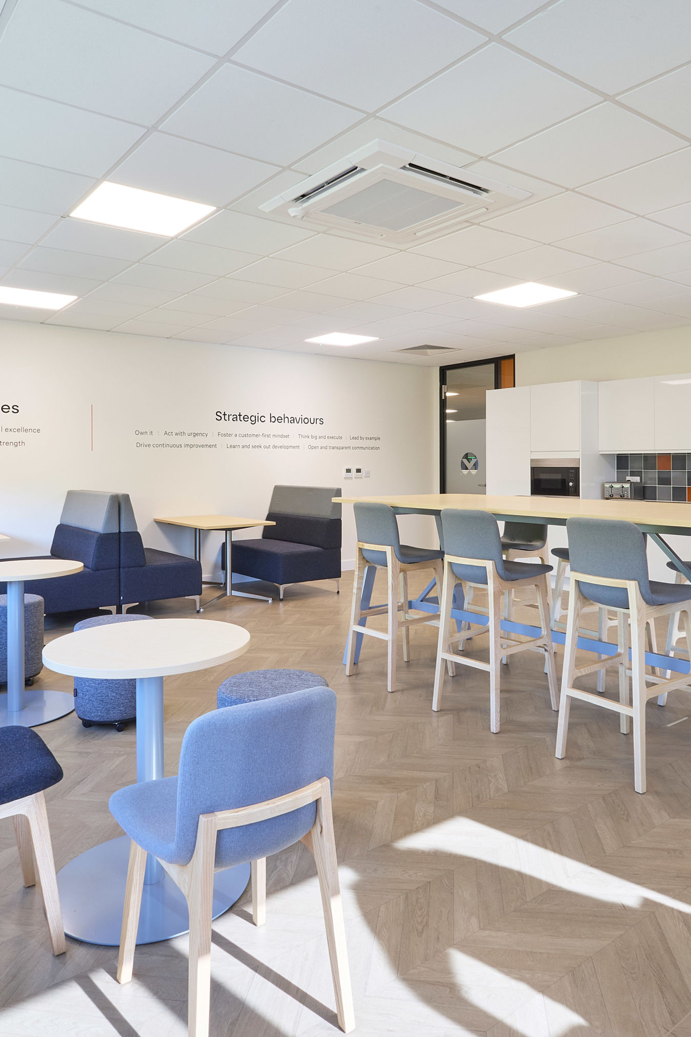 spacious staff room with a large high-top table, various seating areas, and a kitchen on the right