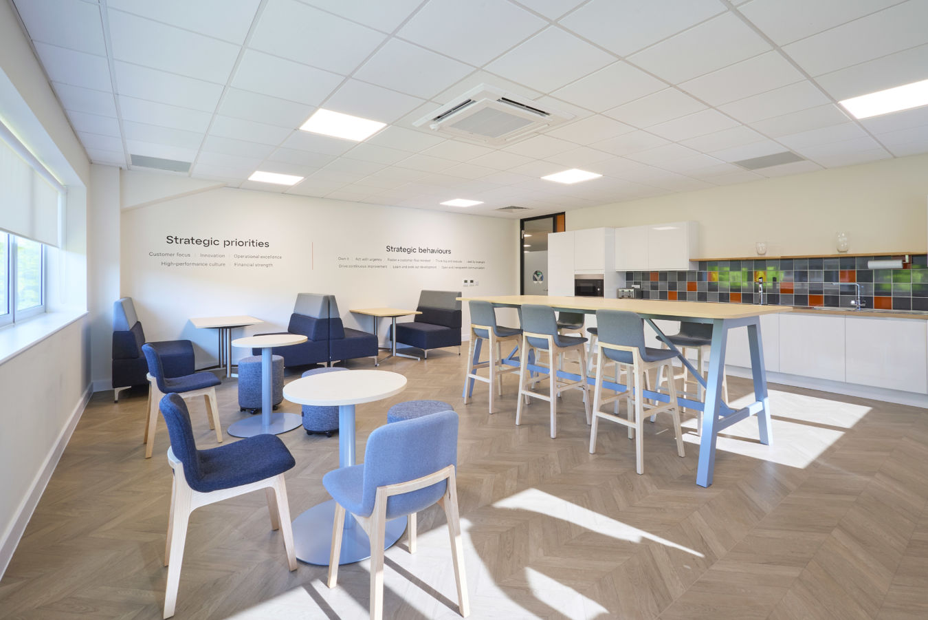 spacious staff room with a large high-top table, various seating areas, and a kitchen on the right
