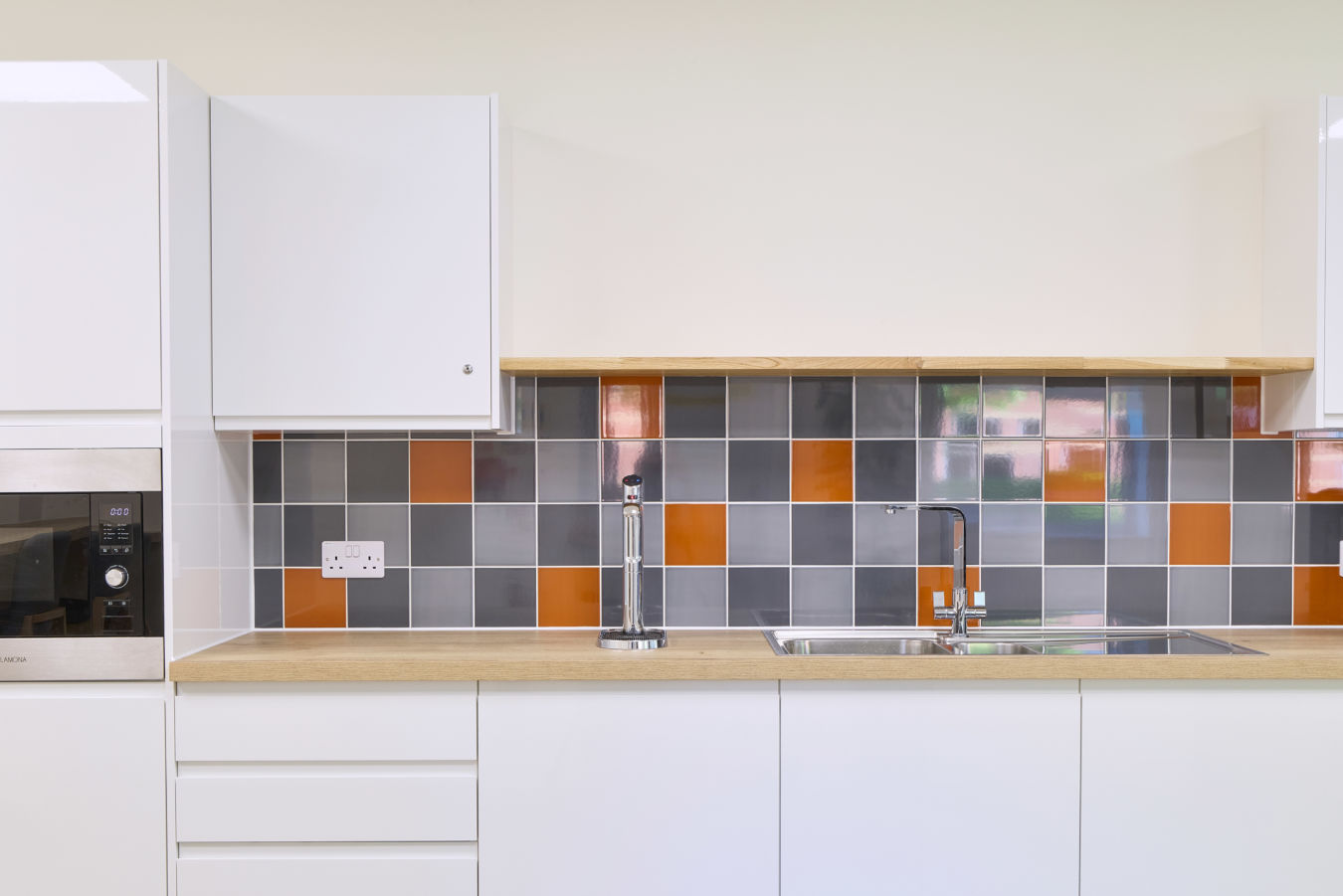 Modern office kitchenette with white cabinetry, wooden countertops, and multicoloured tile backsplash, part of a COEL fit-out project.