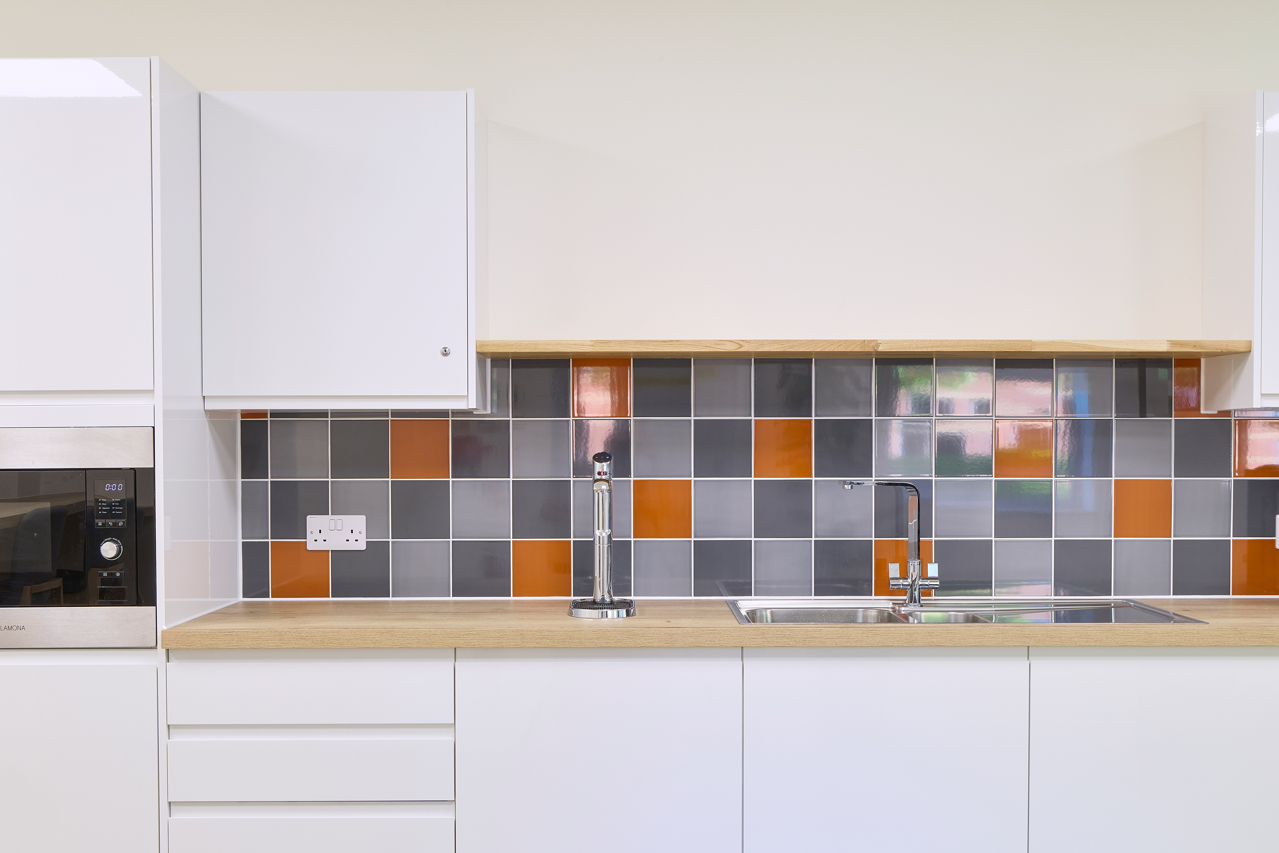 Modern office kitchenette with white cabinetry, wooden countertops, and multicoloured tile backsplash, part of a COEL fit-out project.