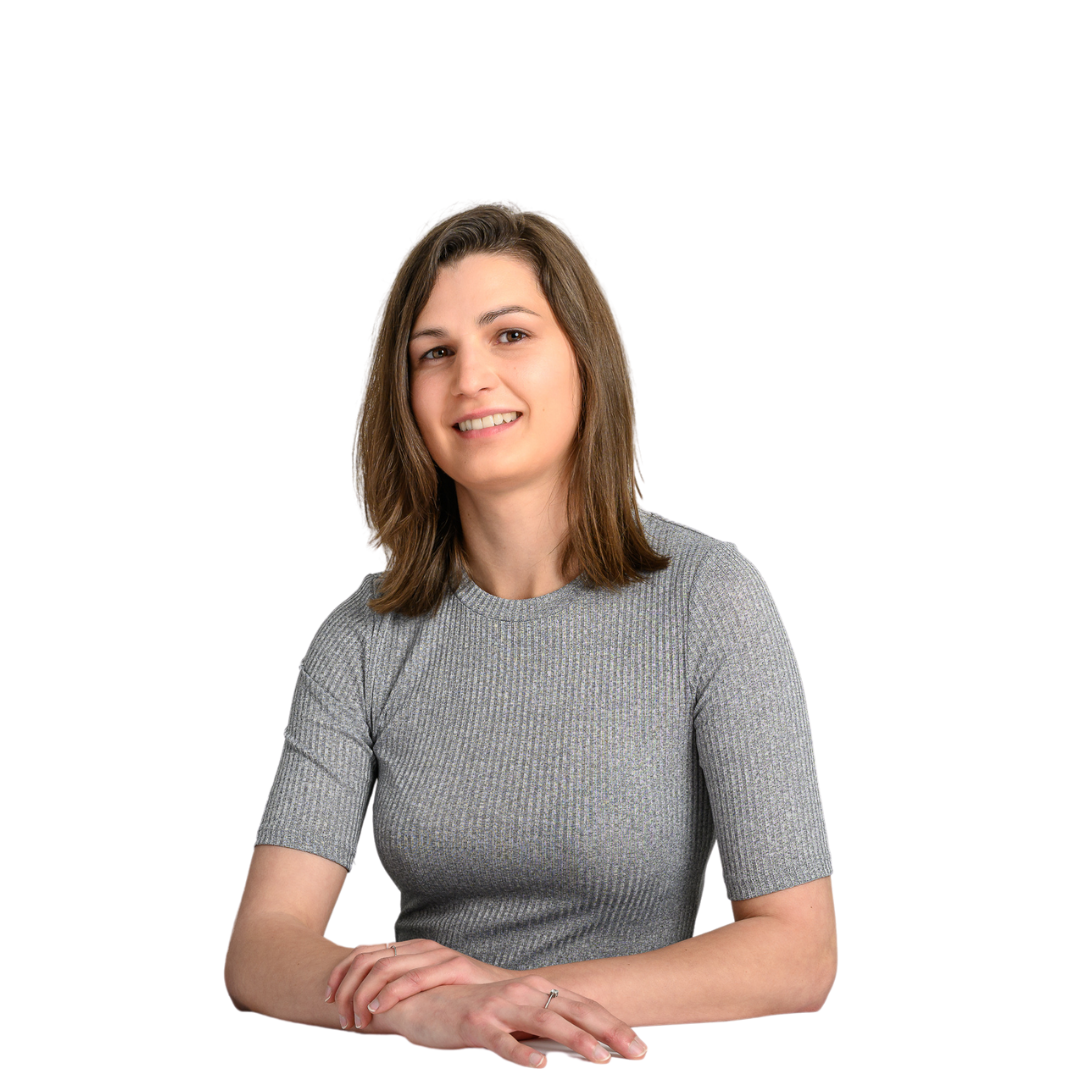 A person wearing a gray, short-sleeved top sits with hands crossed, smiling against a white background.