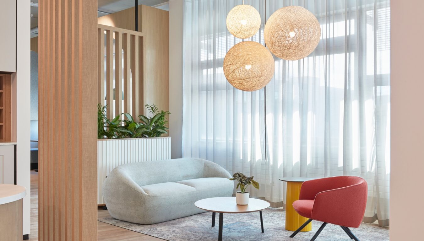 Bright modern seating area with a white curved sofa, round coffee table, red chair, and woven pendant lights