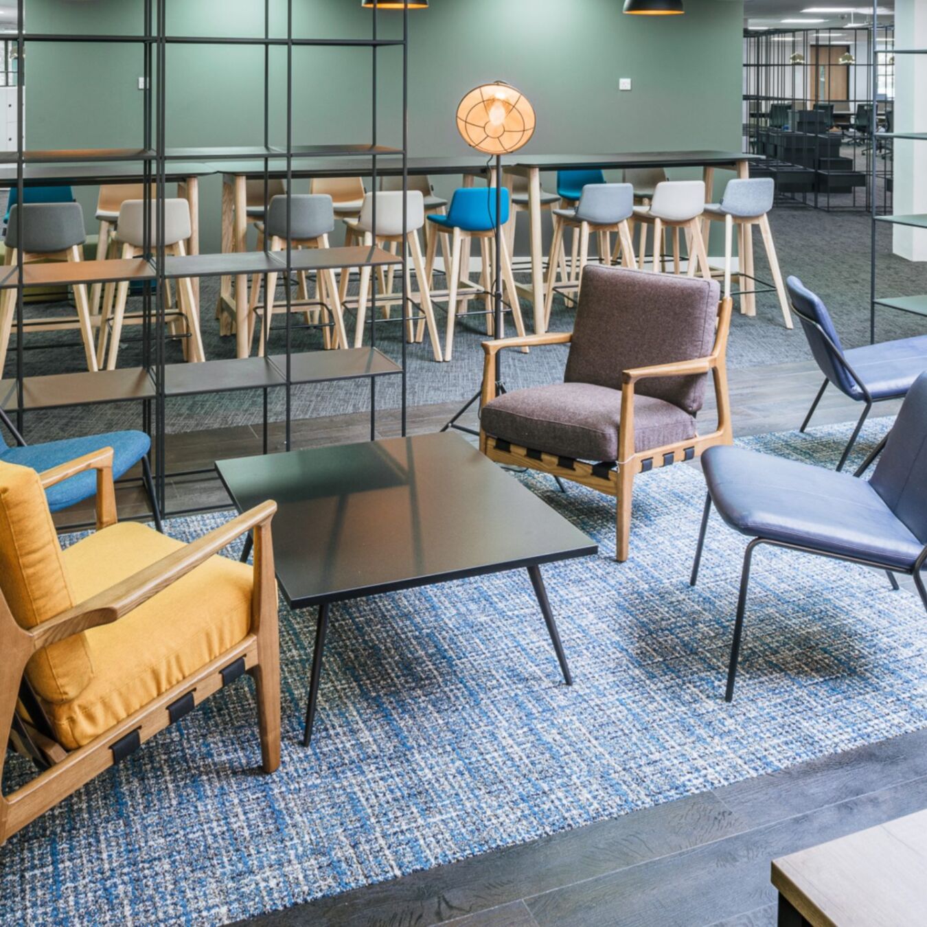 Contemporary lounge with mixed seating, black coffee table, blue rug, and a view into a modern bar-height dining area.