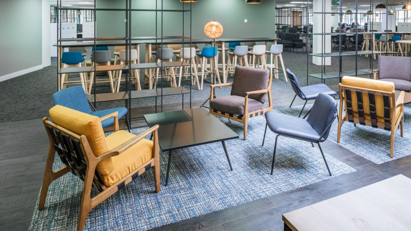 Contemporary lounge with mixed seating, black coffee table, blue rug, and a view into a modern bar-height dining area.