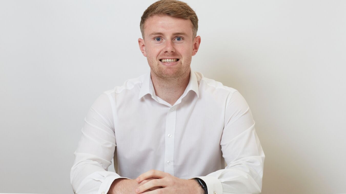 A man in a white shirt smiles while sitting at a table against a plain white background.