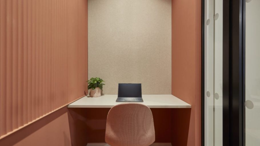 minimalist workspace with a laptop and a plant on a white desk. The room has warm terracotta walls, a textured beige back wall, and modern glass doors