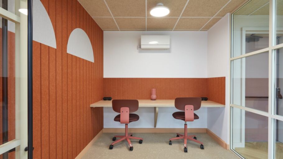 Compact office with two pink chairs at a wooden desk against half-painted terracotta walls. A vase adds decor; ceiling light creates a cozy atmosphere