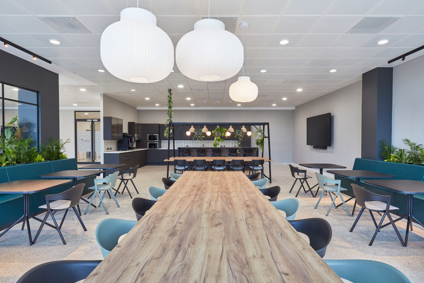 modern office break room with various seating areas, including a long wooden table and booths