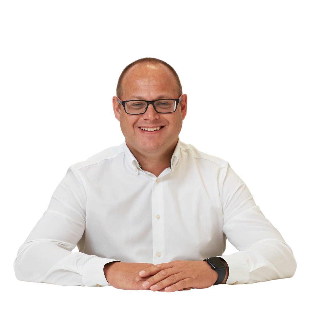 A smiling person in a white shirt sits with hands clasped on a neutral background, wearing glasses and a smartwatch.