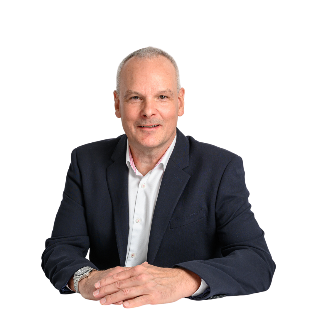 A man in a suit and white shirt sits with folded hands against a plain white background, appearing confident and approachable.