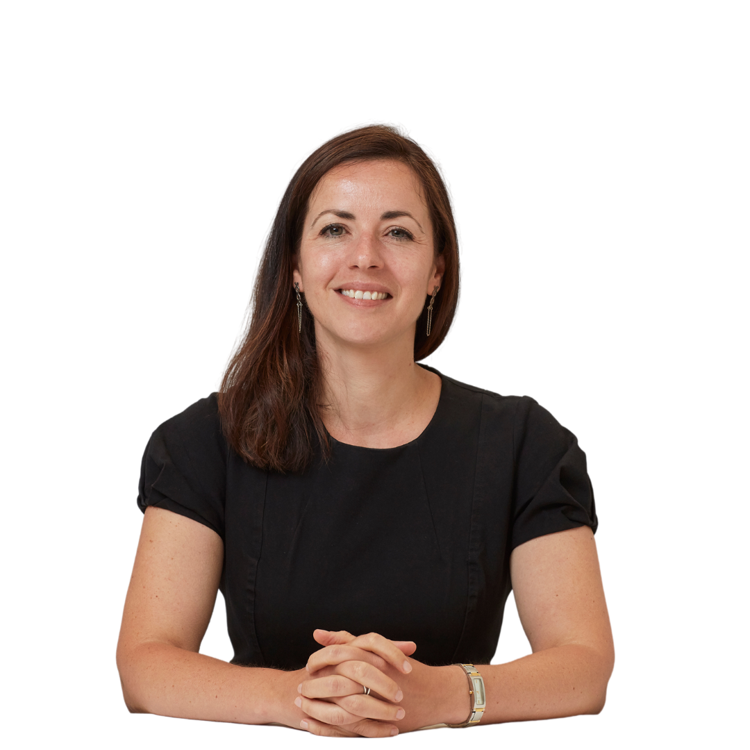A person with long dark hair smiles while sitting with hands clasped on a table, wearing a black shirt, against a white background.