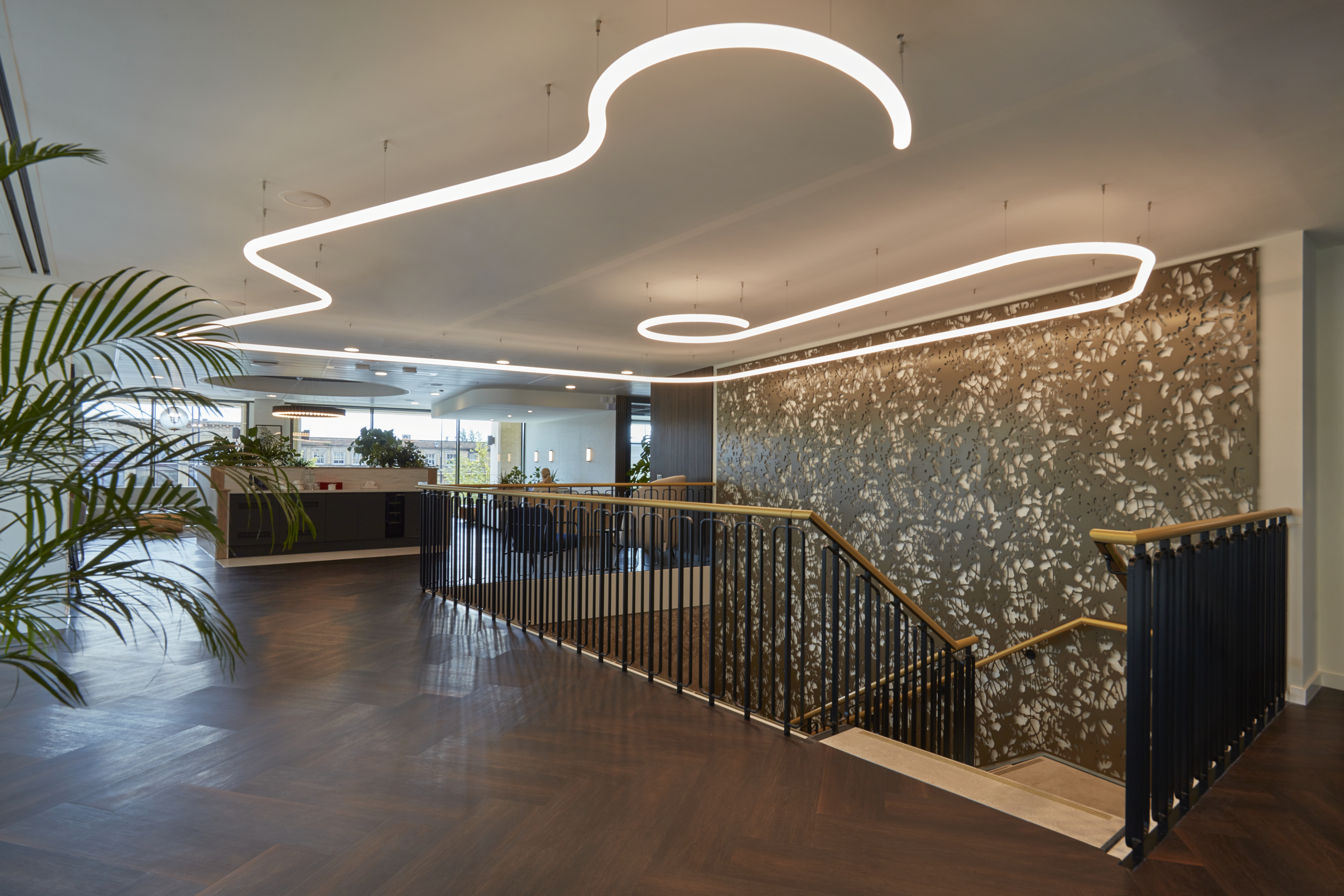 Elegant interior with sculptural ceiling lighting, gold-accented staircase, wood flooring, and decorative wall panels.