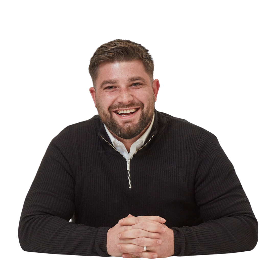 A person in a black zip-up sweater smiles broadly, sitting with hands clasped on a white background.