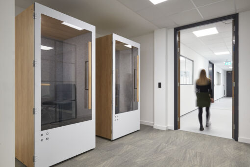 Modern office space with a man working at a desk on the left, under stylish pendant lights. In the background, a kitchenette and plants create a cozy atmosphere