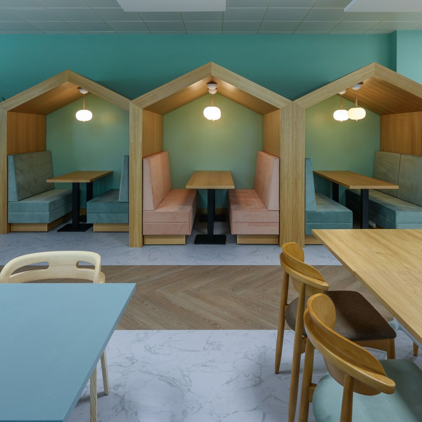 Modern cafe with light wooden tables and pastel seating inside cozy, house-shaped booths. Soft lighting creates a calm, inviting atmosphere