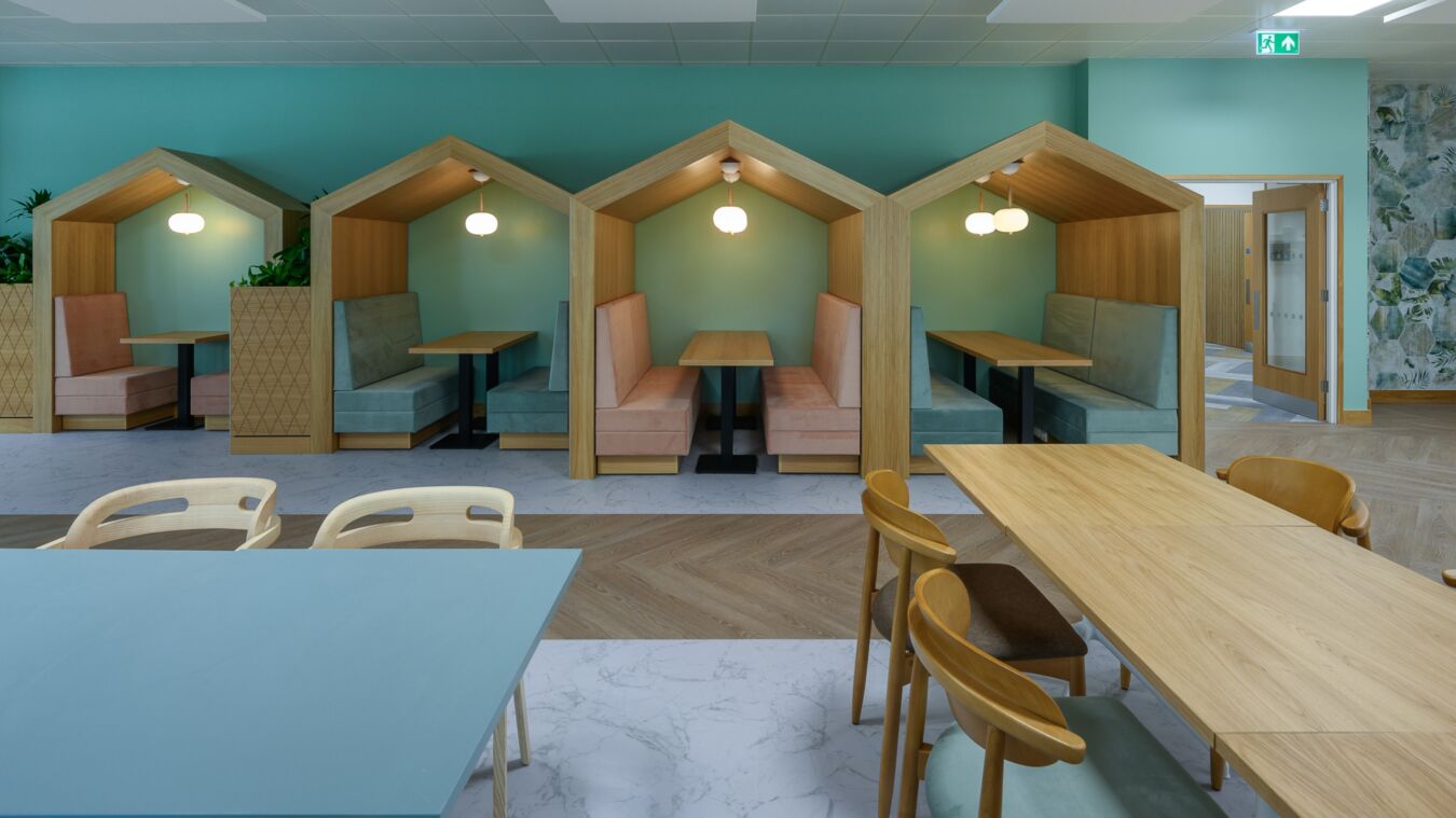 Modern cafe with light wooden tables and pastel seating inside cozy, house-shaped booths. Soft lighting creates a calm, inviting atmosphere
