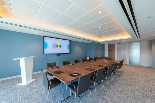 modern conference room with a large wooden table and a screen on a light blue wall
