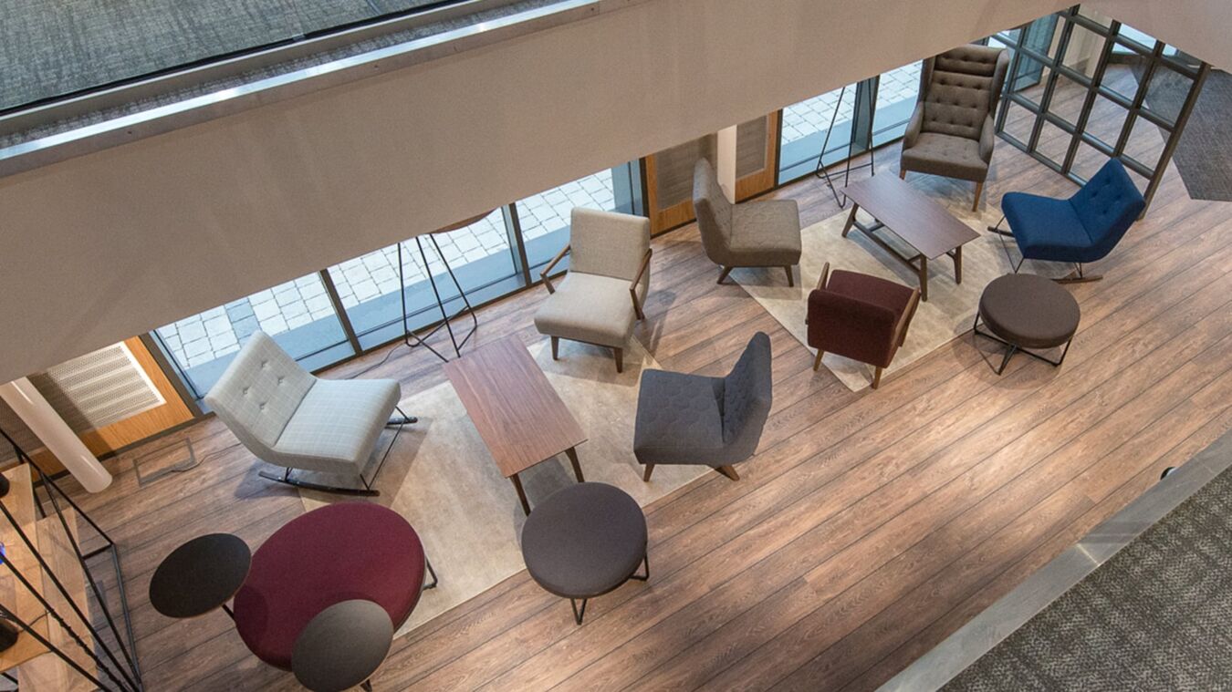 Furniture arrangement features various chairs and tables positioned in a spacious lounge area with wood flooring and large windows overlooking an outdoor space.